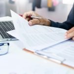 Asian businessman reviewing document reports at office workplace with computer laptop. legal expert, professional lawyer reading and checking financial documents or insurance contract